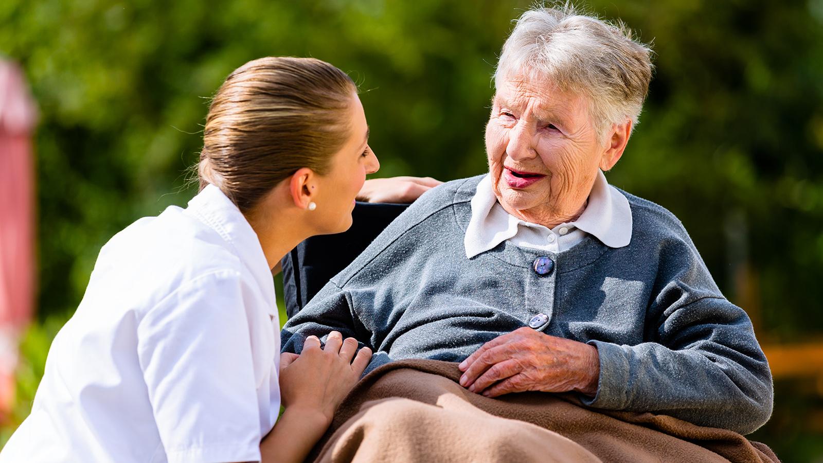 Eine Pflegerin unterhält sich mit einer Patientin im Rollstuhl.